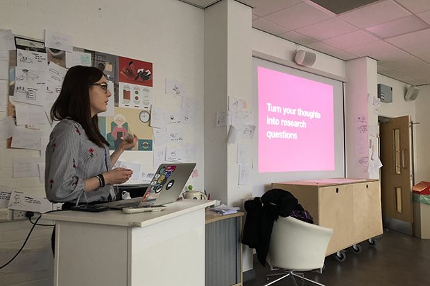 A student standing at a lectern delivering a presentation. On the screeb are the words: Turn your thounghts into research questions