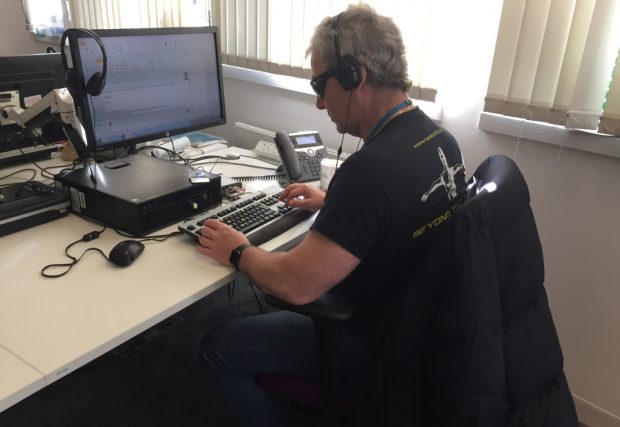 A user of assistive technology at his desk. He is wearing an assistive technology headset because he is blind.