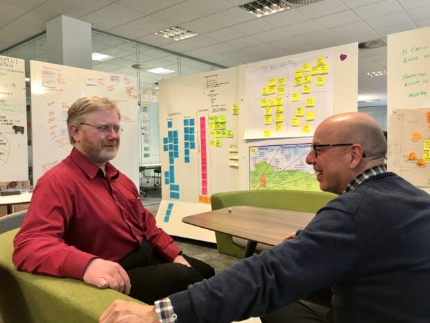 Sean seated on the right talking with colleague Barry seated on the left in an open modern office space