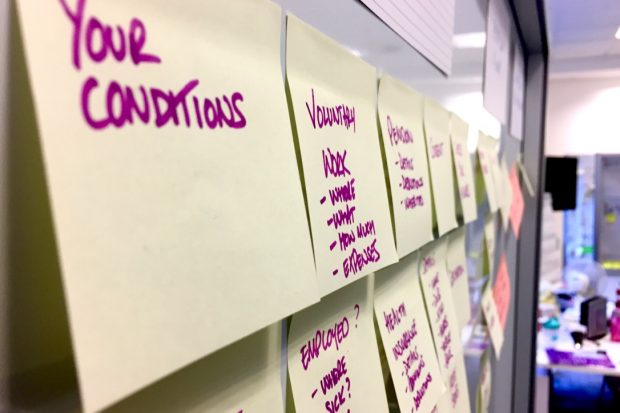 Post-it notes on a whiteboard with writing on including 'your conditions', 'voluntary work', 'employed?', health insurance'