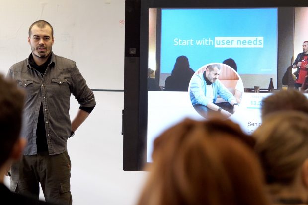 Craig Abbott talking to a group of people about accessibility. On the display screen next to him is a presentation slide with the words 'Start with user needs' written on it.