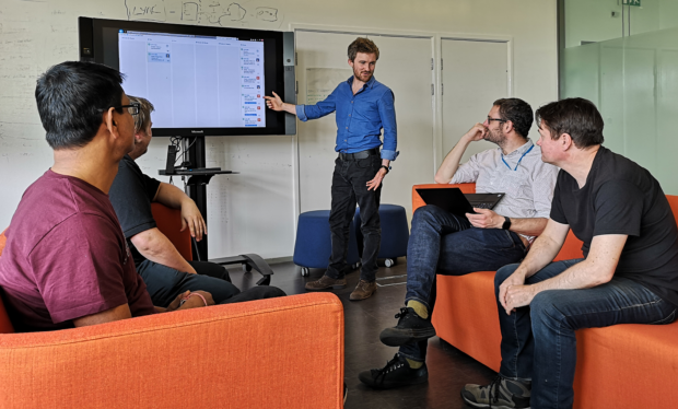 Will at an interactive screen discussing work with colleagues in the tech hub