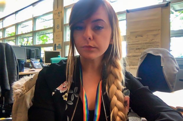 Amy Kiloran sat at a desk looking at the camera wearing a rainbow lanyard