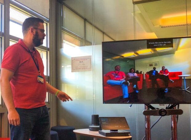 Matthew Walton in front of a TV display screen showing 4 colleagues in a different location during a virtual meeting