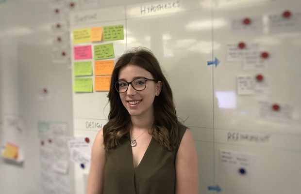 Mel Cotcher standing in the office in front of a whiteboard with post-it notes stuck on it