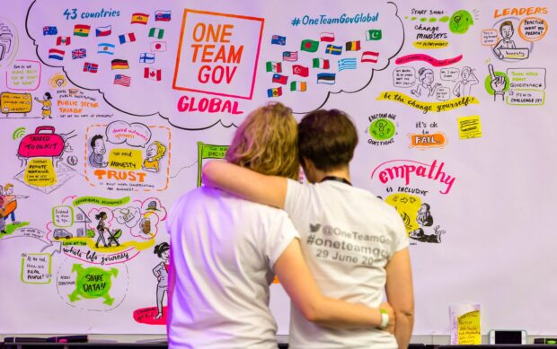 2 people hugging in front of a OneTeamGov colourful display