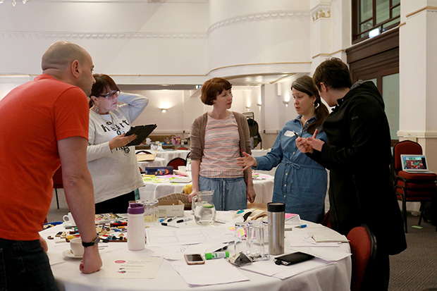 Jacinta Mellinger, DWP service designer discusses ideas with four colleagues at a table full of materials at GovJam Blackpool