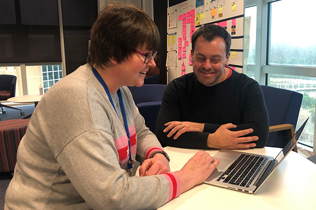 Business Analyst Kathryn Baxendale sits at a table in front of a MacBook computer with DWP Digital content designer Dan Ashworth