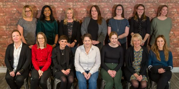 The 14 women taking part in DWP Digital's Digital Voices programme shown in two rows. Seven women are sitting down and Seven are standing up behind them.