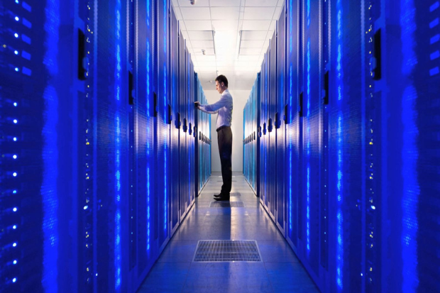 A man is standing in a corridor with large computer servers on each side of him