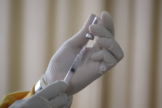 A needle and vaccine are held by someone wearing a latex glove
