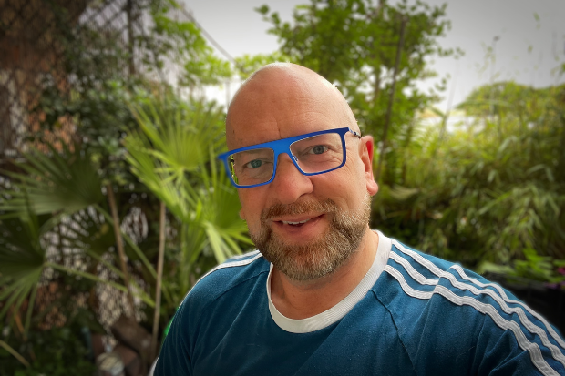 A man wearing blue-framed glasses smiles at the camera