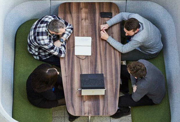 Ariel shot of four people sitting around a meeting table with a laptop on it