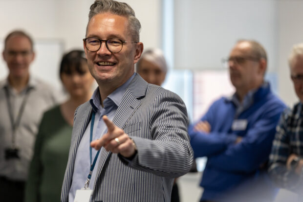 Richard smiling and pointing at colleagues in a relaxed meeting setting.